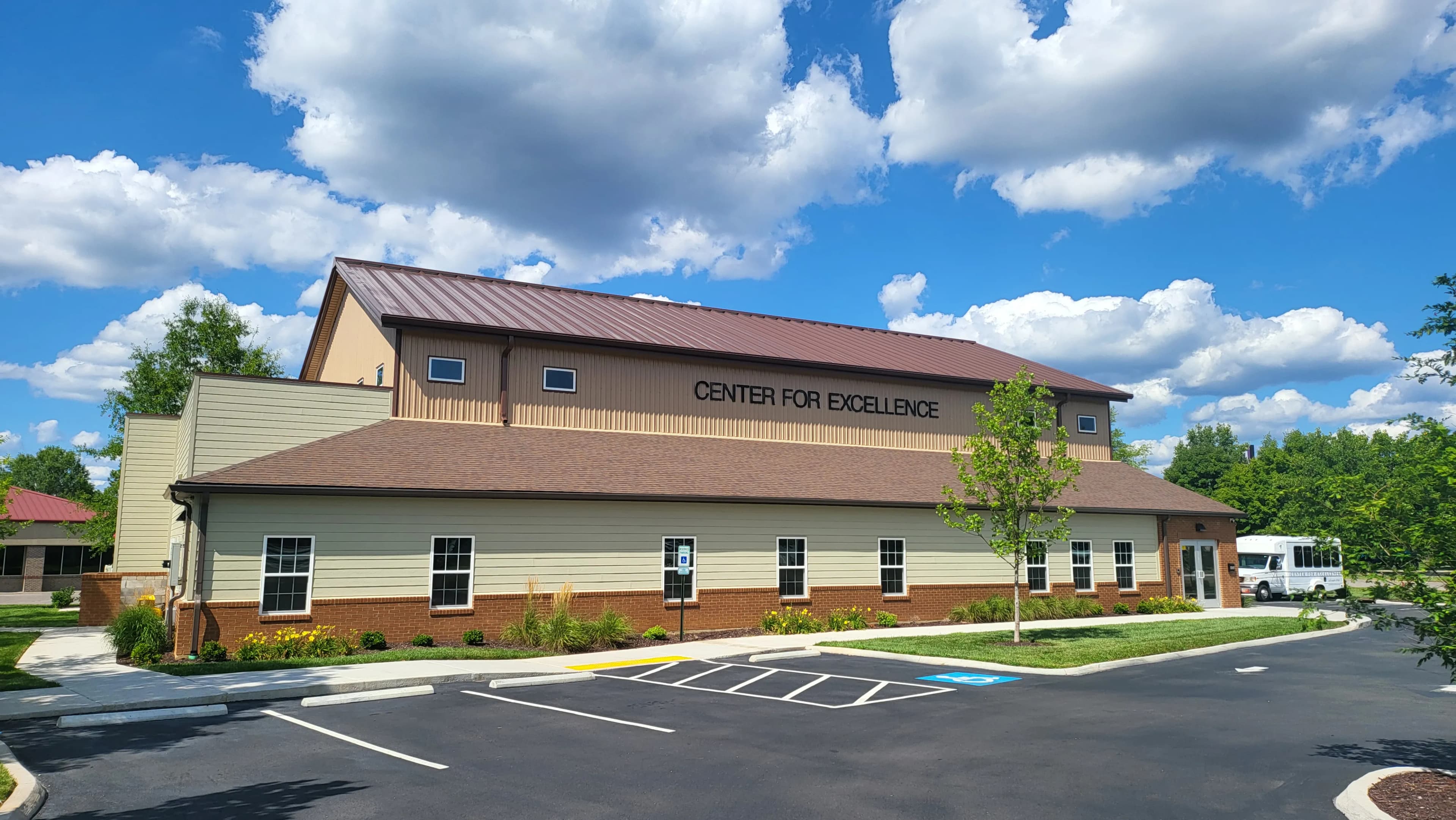 Tan double story building with the words Center For Excellence on the front with a darker brown metal roof